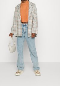 Kostium w kratę w kolorach białym, zielonym i czerwonym; pomarańczowy krótki sweter; jasnoniebieskie jeansy o prostym kroju; biała torba; beżowe sneakersy.