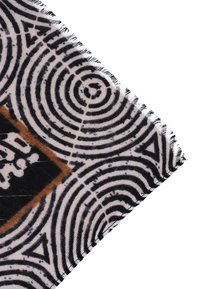 Tessuto a motivi in bianco e nero con disegni circolari, caratterizzato da bordi sfilacciati e un rettangolo marrone a contrasto con del testo.