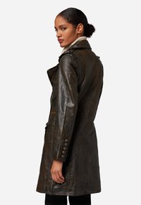 Brun läderjacka med en figursydd design, stor krage och knäppdetaljer. Har en texturerad yta och snedställda sidofickor.