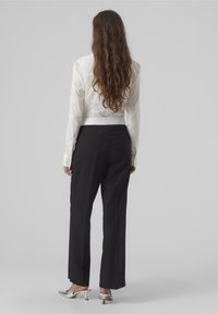 Blusa bianca cropped con maniche lunghe e dettagli con cintura, abbinata a pantaloni neri a vita alta e scarpe con tacco argentate.