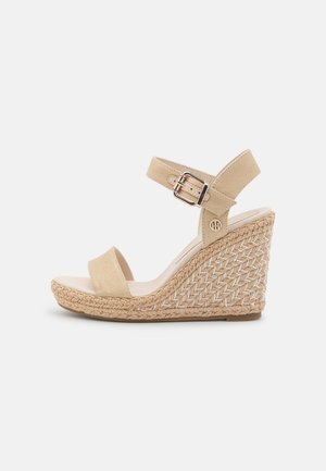 Beige kile-sandal med flettet jute-platform, åben tå og justerbar ankelrem med metalspænde.