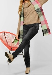 Avslappnad outfit med en taupefärgad stickad tröja, mönstrade svarta jeans och ljusbeige klackar, kompletterad med en flerfärgad rutigt sjal.