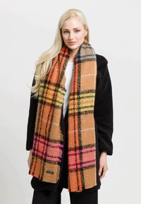 Brunternede plaid-scarf med livlige orange, pink og grønne detaljer. Blød tekstur og frynser i kanten, båret over en sort frakke.