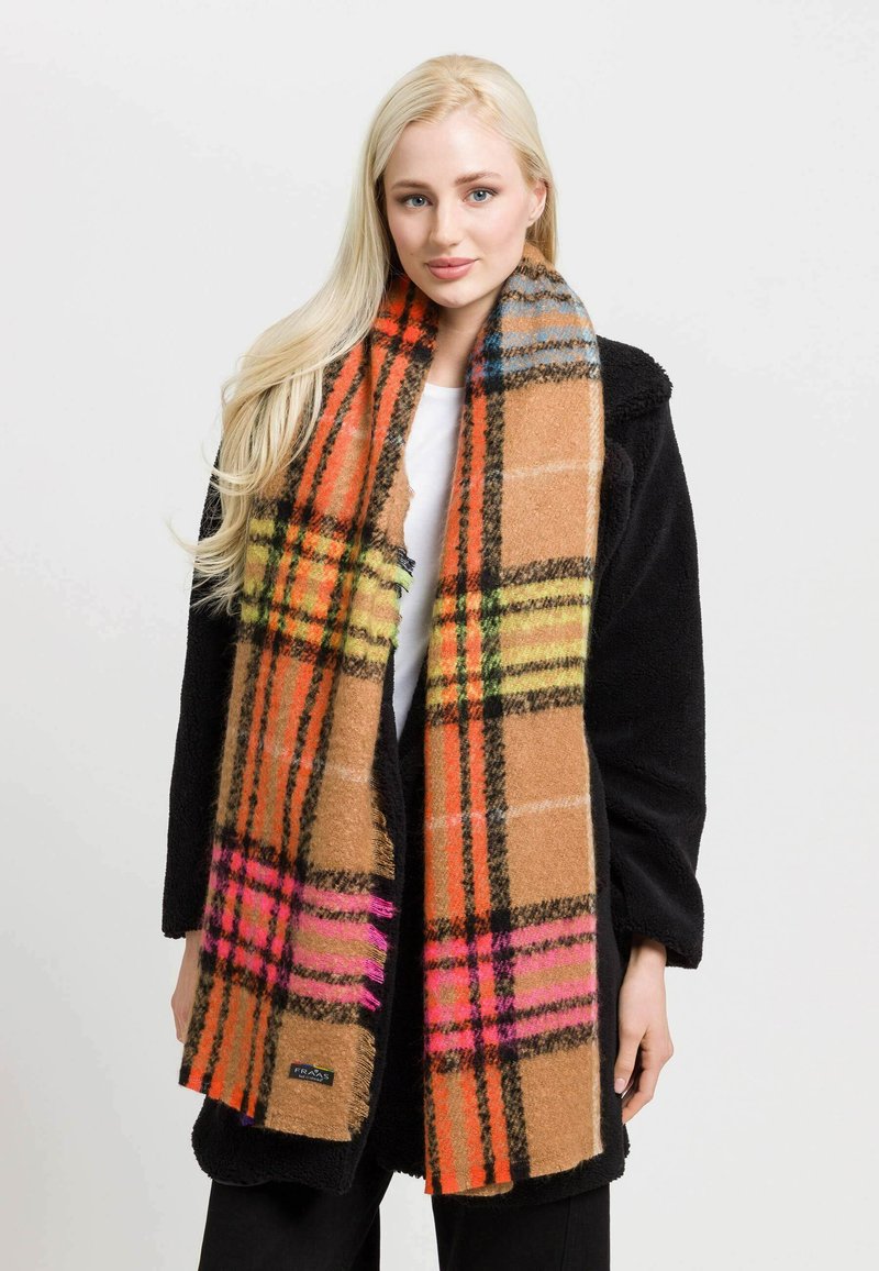 Brunternede plaid-scarf med livlige orange, pink og grønne detaljer. Blød tekstur og frynser i kanten, båret over en sort frakke.