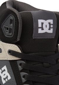 Baskets montantes noires en mesh et matériaux synthétiques. Présentent un logo proéminent, des accents gris et des lacets noirs. Construction texturée.