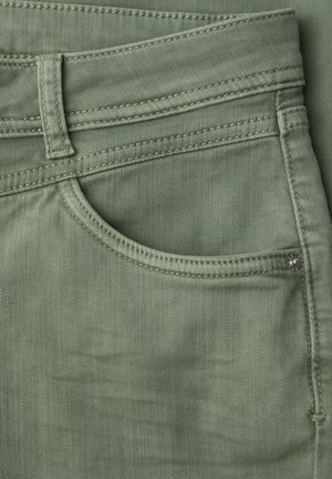Gros plan sur la poche d'un pantalon en denim vert avec passants pour ceinture et détails de coutures visibles.