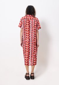 Kurzärmliges, midi-langes Kleid in Pink mit einem geometrischen Muster in Rot und Schwarz. Hergestellt aus strukturierter Stoff; hat einen geraden Schnitt und einen Kragen.