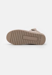 Chaussures beiges avec une semelle en caoutchouc texturé, présentant des rainures horizontales et un profil plat. Comprend des éléments décoratifs sur le dessus.