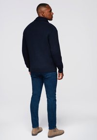 Maglione a coste navy con colletto alto, abbinato a jeans blu scuro e stivali Chelsea beige, visto da dietro.