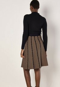 Personne portant un haut noir à manches longues côtelé et une jupe marron longueur genoux avec des rayures verticales noires et des motifs géométriques, vue de dos.