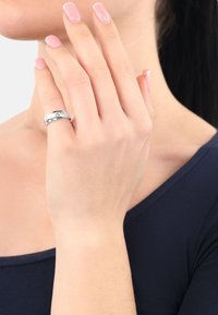 Sterling silver ring med en slät band, med en liten ädelsten som accent. Buren på en hand med ljus hy och manikyrerade naglar.