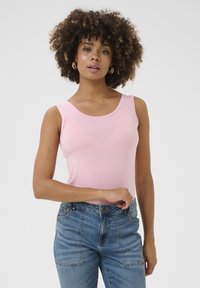 Rožinė prie kūno priglundanti marškinėlė su apvaliu iškirpimu, pagaminta iš minkštos medžiagos. Dėvimi su mėlynomis aukštu juosmeniu džinsais, turinčiais priekinės kišenes.