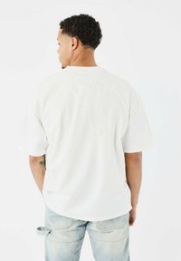 Camiseta blanca de manga corta con un sutil bordado de cactus en la parte posterior y las mangas, hecha de una tela ligera y suave.