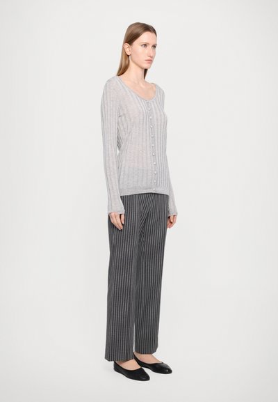 Vaaleanharmaa röyhelö cardigan, jossa on napit, yhdistettynä musta-valkoisiin raidallisiin leveälahkeisiin housuihin ja mustiin flats-kenkiin.