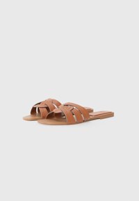 Sandalias planas marrones con amplias hendiduras, fabricadas en material sintético. Presentan una textura suave y un diseño minimalista con una suela plana.