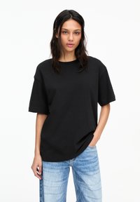 T-shirt noir oversize en coton, à manches courtes et col rond, associé à un jean en denim bleu clair.