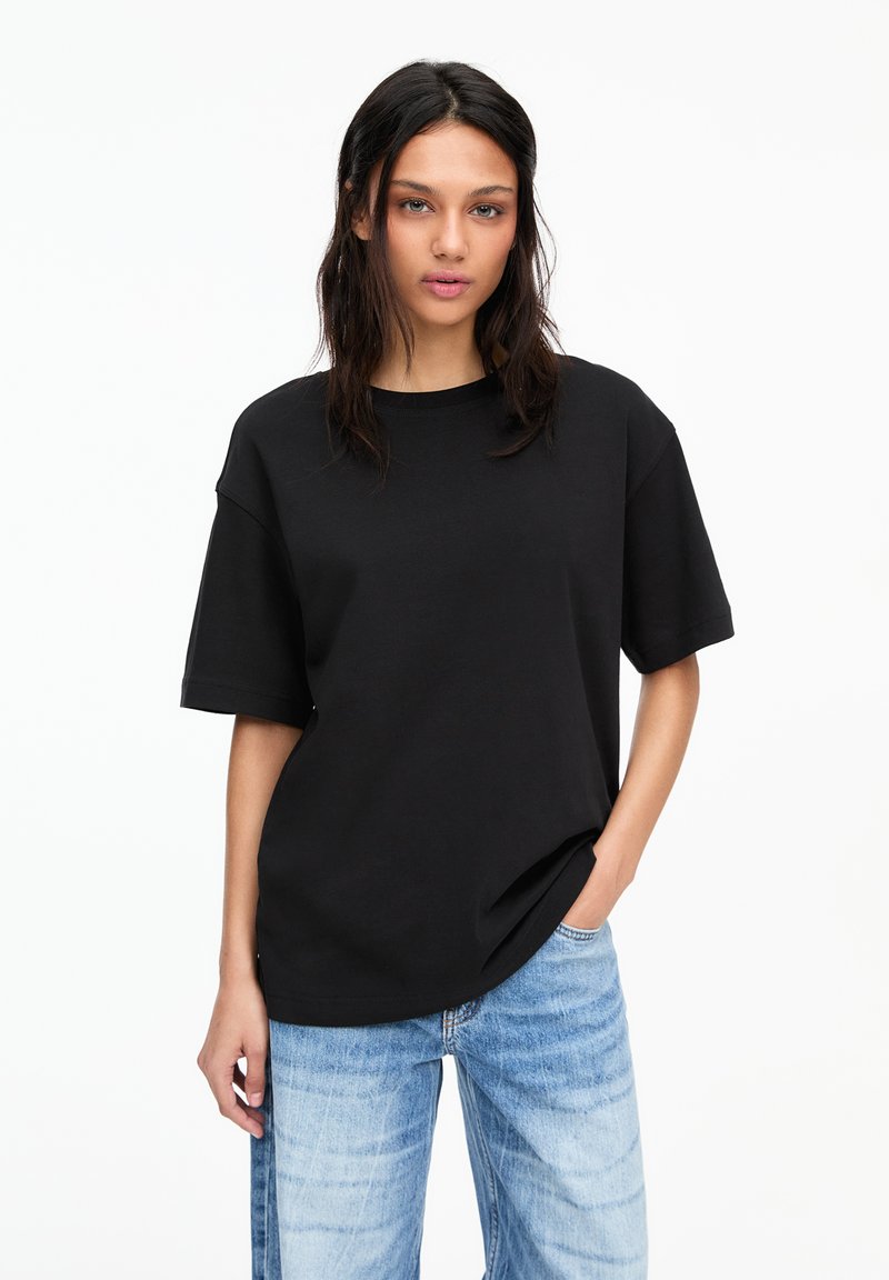T-shirt noir oversize en coton, à manches courtes et col rond, associé à un jean en denim bleu clair.