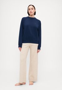 Sudadera azul marino con cuello redondo y puños acanalados, combinada con pantalones de pierna ancha de color beige claro. La tela parece suave con un diseño minimalista.
