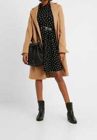 Kameliintakki mustan pilkullisen mekon päällä, vyötetty mustalla vyöllä. Musta olkalaukku ja nilkkurit täydentävät asun.