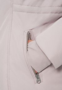 Světle růžová bunda s kapsou na zip a stříbrným zipem, hladkou texturou a těsným střihem.