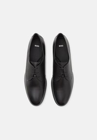 Black leather dress shoes with smooth and textured finishes, featuring laces and a minimalist design. Logo "BOSS" visible on the insoles.