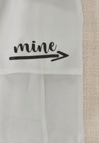 Weißer Stoff mit schwarzem, kursiv geschriebenem Text "mine", gefolgt von einem Pfeil, mit glatter Textur und einfachem Design.