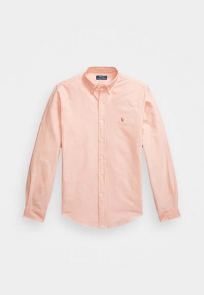 Šviesiai rožinė mygtukinė marškiniai, pagaminti iš medvilnės. Turi klasikinį apykaklę, ilgomis rankovėmis ir nedidelį logo siuvinėtą ant krūtinės.