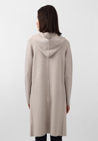 Cardigan lungo beige chiaro con cappuccio, realizzato in tessuto morbido, caratterizzato da un taglio dritto e una cucitura centrale, che arriva a metà coscia.