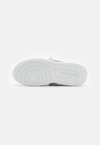 White rubber sneaker sole with circular tread pattern and grooves. Features a small logo imprint near the heel area.
