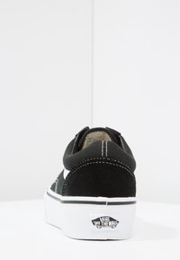 Czarno-białe trampki Vans widziane z tyłu, z białymi szwami i logo "Vans Off The Wall" na podeszwie.