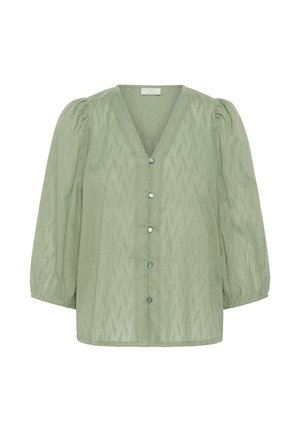 Blouse vert clair avec des manches trois-quarts bouffantes, motif en zigzag gaufré, décolleté en V, et une rangée de cinq boutons assortis sur le devant.