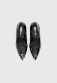Scarpe col tacco alto in vernice nera con punta affilata, dettagli ritagliati e accenti metallici. Le etichette all'interno indicano "Karl Lagerfeld."
