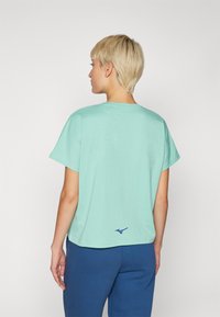 Myntgrønn bomulls t-skjorte med en løs passform, korte ermer og en marineblå logo på baksiden. Glatt tekstur og enkelt design.