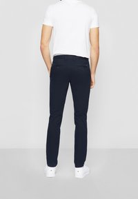Marineblauwe slim-fit broek met een gladde textuur, voorzien van twee achterzakken, gedragen met een wit T-shirt en witte sneakers.