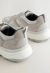 Grau Wildleder- und Mesh-Sneaker mit einer gepolsterten weißen Sohle, ausgestattet mit einem gepolsterten Schaft und Schnürsenkeln, die für Komfort und Atmungsaktivität konzipiert sind.
