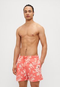 Bañador de coral con patrón floral blanco, cintura elástica y cordón. Bolsillos laterales y detalle del logo en la pierna izquierda.