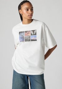 White oversized t-shirt made of cotton, featuring a graphic collage with nature and abstract images in soft colors, centered text below.