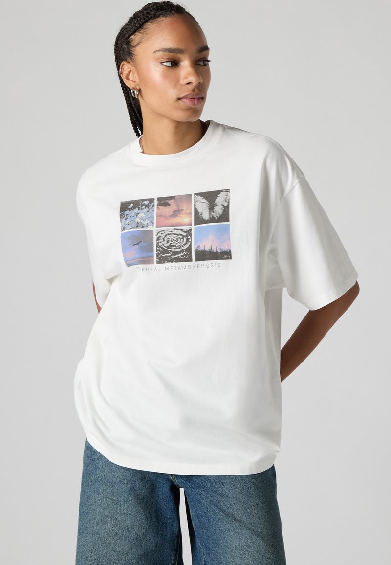 White oversized t-shirt made of cotton, featuring a graphic collage with nature and abstract images in soft colors, centered text below.