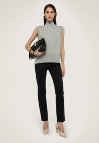 Grå ärmlös polotröja med ribbad nederkant, tillsammans med svarta tighta byxor och nakna högklackade skor, håller en svart handväska.