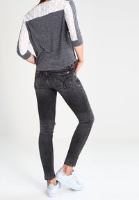Graue Spitze und Jersey-Oberteil mit rundem Ausschnitt, kombiniert mit dunkelgrauen Skinny-Jeans und weißen Turnschuhen, von hinten betrachtet.