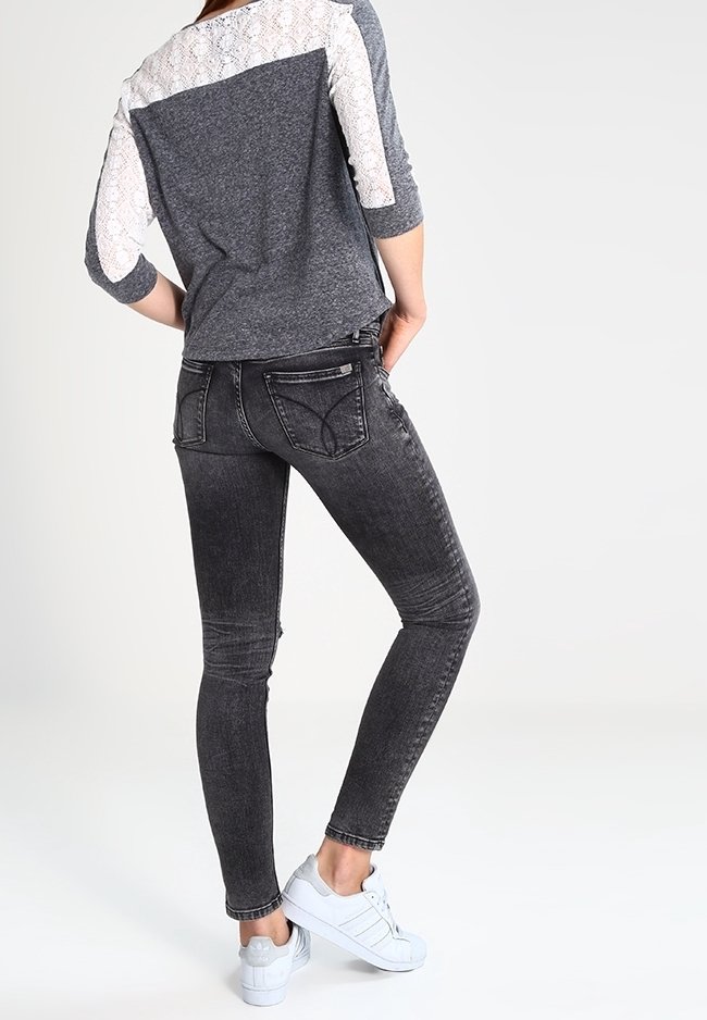Graue Spitze und Jersey-Oberteil mit rundem Ausschnitt, kombiniert mit dunkelgrauen Skinny-Jeans und weißen Turnschuhen, von hinten betrachtet.