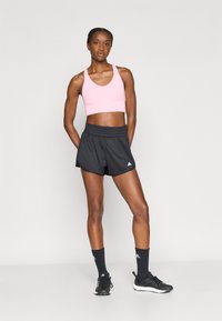 Różowy sportowy biustonosz i czarne szorty z elastycznym pasem. Czarne skarpetki i sneakersy, prezentujące sportowy design i funkcjonalne materiały.