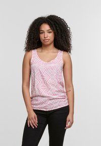 Rosa tanktop med geometriske hvite mønstre, v-utringning og brede stropper. Stoffet ser mykt ut med en glatt tekstur. Satt sammen med svarte bukser.