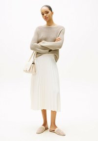 Beige gestrickter Pullover mit langen Ärmeln, weißer plissierter Midirock und hellbeige geflochtenen Slipper. Die Accessoires umfassen eine kleine cremefarbene Handtasche.