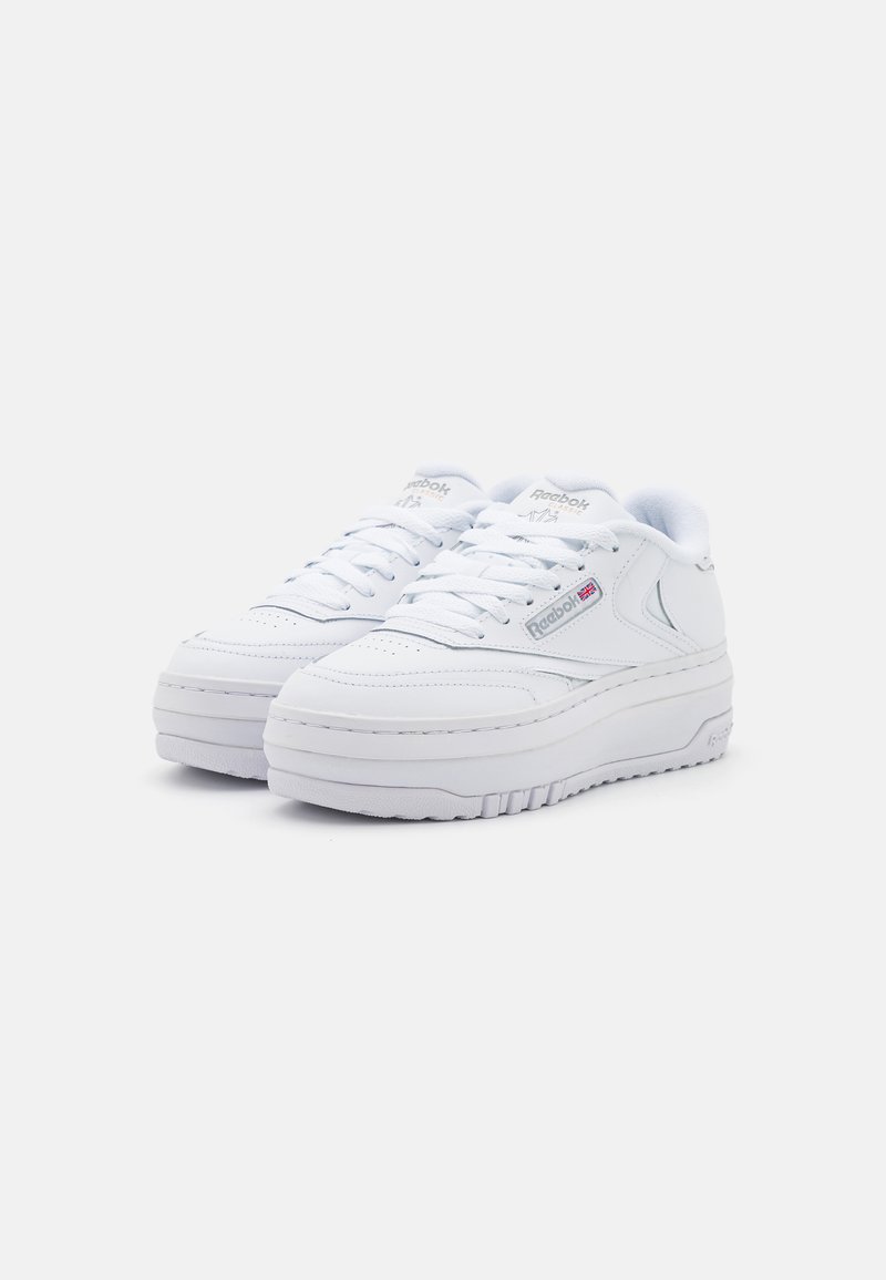 Baskets en cuir blanc avec une languette rembourrée, lacets ronds, semelle épaisse et étiquette logo sur le côté. Présente un design minimaliste et des accents cousus.