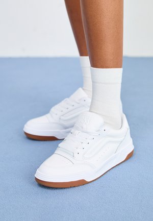 Białe skórzane sneakersy z perforowanymi detalami, jasnoniebieskim przeszyciem i gumową podeszwą. Połączone z białymi skarpetkami do kostek.