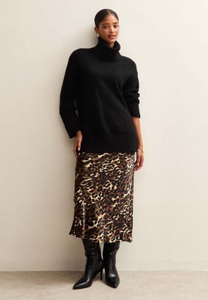 Jersey de cuello alto negro con ajuste holgado, combinado con una falda midi de estampado de leopardo y botas negras hasta la rodilla, sobre un fondo neutro.