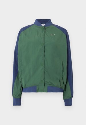 Zeleni in mornarsko modri vetrovka z ovratnikom, zapiranjem na pritrdilne gumbe in belim logotipom Nike v obliki kljukice na prsih. Lahka, gladke teksture.