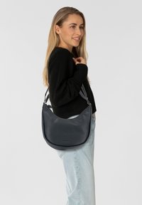 Hobo-tas gemaakt van soepel donker leer, met een gebogen ontwerp, verstelbare schouderband en subtiele branding aan de voorkant.