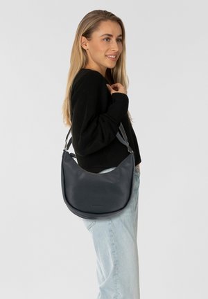 Sac hobo en cuir lisse et foncé, avec un design courbé, une bandoulière ajustable et un branding subtil à l'avant.